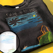 Load image into Gallery viewer, folded black crew neck sweatshirt with custom embroidery of child's drawing of a father and son fishing on a lake next to a cabin
