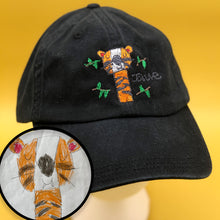 Load image into Gallery viewer, black hat with custom embroidery of child's drawing of an orange tiger with a big smile and closed eyes, surrounded by green leaves
