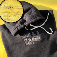 Load image into Gallery viewer, black hoodie with custom embroidery of cream color musical notes playing "summertime" song, drawn by a child