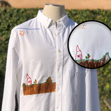 Load image into Gallery viewer, white button up shirt with embroidery of brown and red house on mannequins right hip and yellow sun and sky on wearers right shoulder
