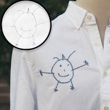Load image into Gallery viewer, potato stick figure man with a big smile embroidered onto chest of white button up shirt in color changing blue and pink thread 

