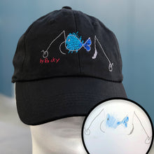 Load image into Gallery viewer, Black baseball hat with custom embroidery of kids drawing of a blue fish surrounded by gray fishing hooks
