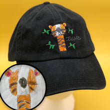 Load image into Gallery viewer, black hat with custom embroidery of child&#39;s drawing of an orange tiger with a big smile and closed eyes, surrounded by green leaves
